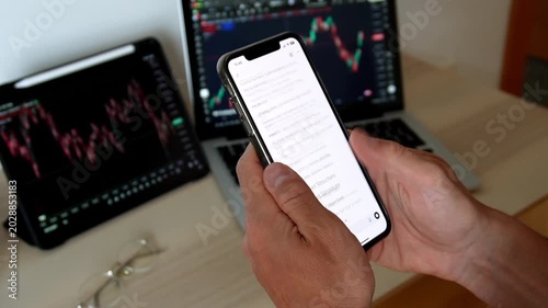 Man hands holding smartphone with AI chatbot showing trading analysis text in front of stock market monitors with charts. Concept of fintech, AI trading assistant, investment and market analysis.