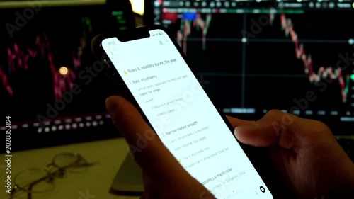 Man hands holding smartphone with AI chatbot showing trading analysis text in front of stock market monitors with charts. Concept of fintech, AI trading assistant, investment and market analysis.