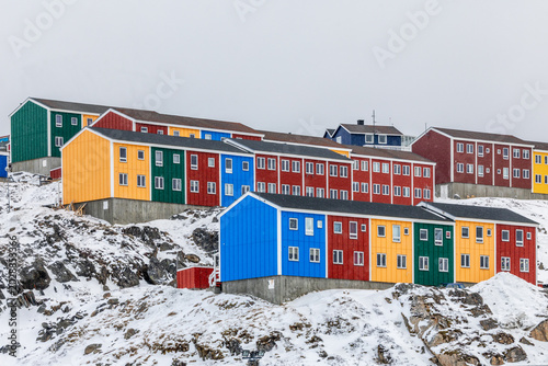 Bright red, orange, green and blue residential buildings with snow-covered rocks and cloudy sky in a Greenlandic town, Sisimiut, Qeqqata, Greenland