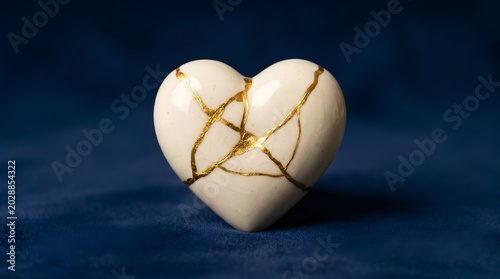 Broken white porcelain heart repaired with gold kintsugi technique for emotional healing resilience and soul restoration concept

