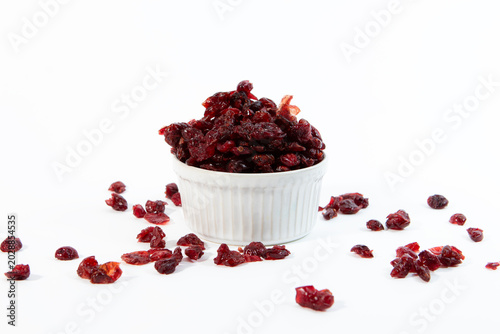 A white ceramic cup filled with dried cranberries with a few extra berries scattered around the base on a clean white background
