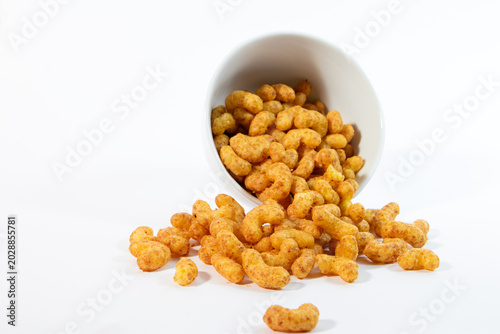 Crunchy peanut flips snacks spilled out from a tipped white ceramic cup onto a clean white background