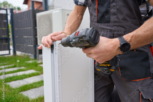 Man fastens white drawer side with cordless drill near grass outside