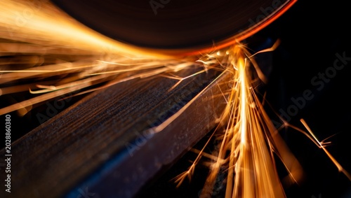фотографія Abstract macro long-exposure shot of a grinding wheel edge on a steel surface, capturing dramatic streaking orange spark light trails against a dark background