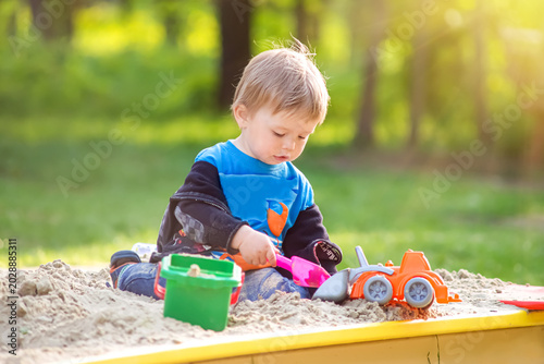 Bild auf Leinwand Toddler boy playing with plastic truck and shovel in sandbox at playground