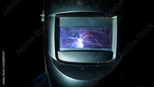 Schilderij op canvas Close-up of a well-used welding helmet lens reflecting a vivid purple-blue welding arc