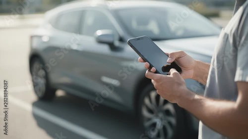 Medium shot of a person activating a rental car insurance policy on an app focusing on the phone screen with soft focus on the vehicle behind.