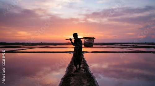 Salt Farmer Worker Walking Across Salt Ponds at Sunset Silhouette