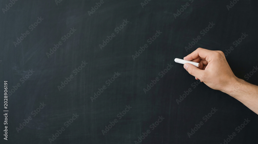 Naklejka premium A hand holding chalk poised to write on a blank blackboard, evoking education and creativity