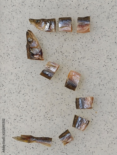 Creative flat lay composition of the number 5 formed by pieces of sliced dried fish, such as smelt or vendace, arranged on a light grey speckled background, showcasing a unique food art concept from
