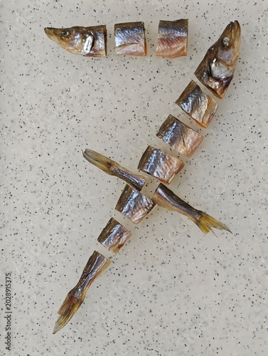 Top-down view of dried and cut smelt fish pieces creatively arranged to form the numeral 7, presented on a speckled light gray and white countertop, emphasizing a unique culinary snack.