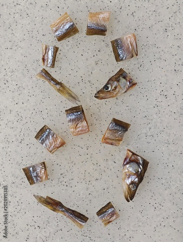 Dried and salted vendace fish pieces, including heads and tails, artfully arranged on a light speckled surface, forming the numeral eight (8), a Ukrainian digit, symbolizing infinity, or success.