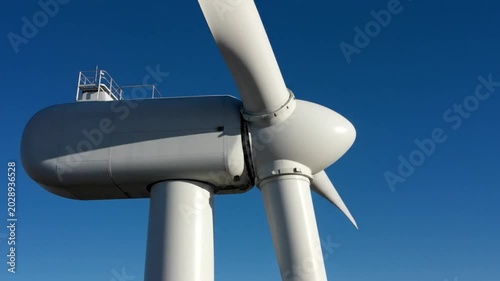 Low angle close-up of a large white wind turbine rotating against a bright blue sky on a sunny day