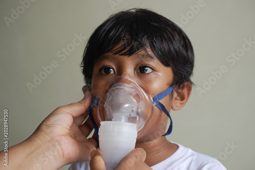 Tableau sur toile Close up young child receiving respiratory treatment, person hand helping to wearing mask, focus on eyes glance and unwell face expression