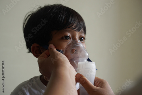Photos Close up young child receiving respiratory treatment, person hand helping to wearing mask, focus on eyes and unwell face expression