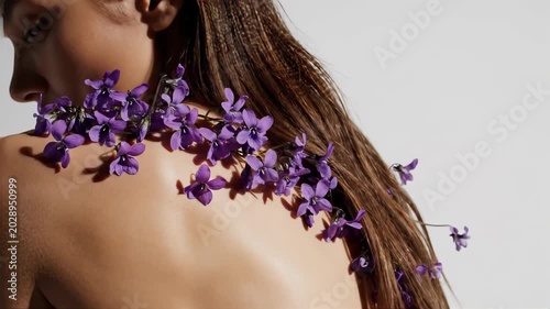 Woman's shoulder with delicate purple flowers cascading over her skin and hair