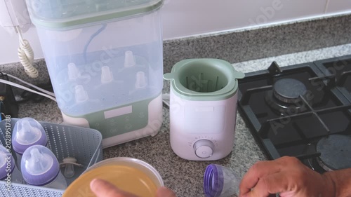 Man's hands mixing formula milk and using an electric warmer to heat the baby bottle in the kitchen