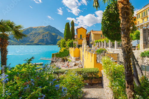 A small beach surrounded by vibrant yellow resort buildings along the shores of Lake Como, at the idyllic Italian village of Varenna, Italy.