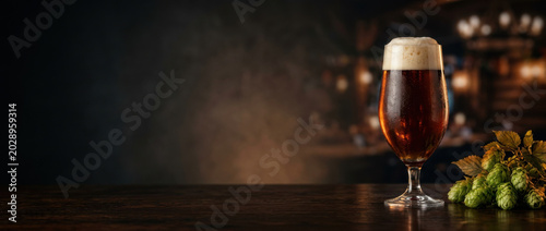 Beer glass dark scene illuminated polished wood ale foam head pub Oktoberfest, beer glass polished wood table dark pub scene, illuminated drink