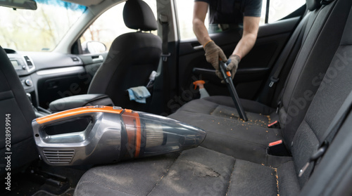 Worker vacuuming crumbs from car back seat with handheld cleaner for auto detailing interior maintenance hygiene service cleanup transport care concept mobile cleaning service workflow