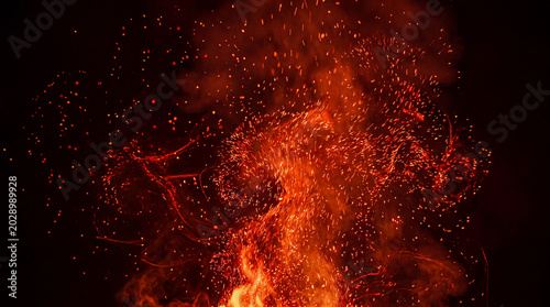 Photos Exploding red-orange fire sparks ignite intensely in a dynamic, fiery swirl against a dark, dramatic abyss background