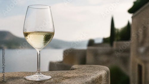 A clear glass of white wine on a stone ledge with condensation.