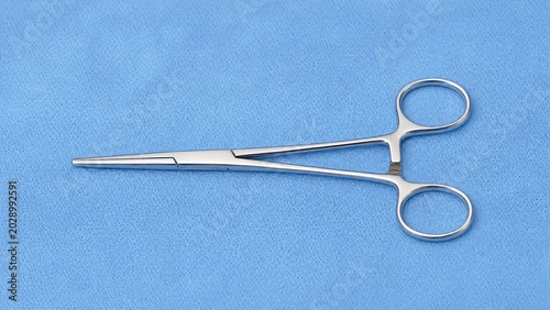 A stainless steel hemostat on a blue surgical drape.