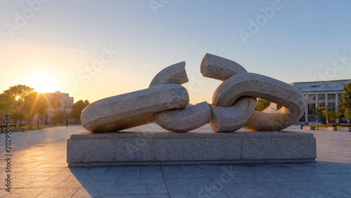 Broken chain sculpture in a public square during morning light, symbolizing freedom.