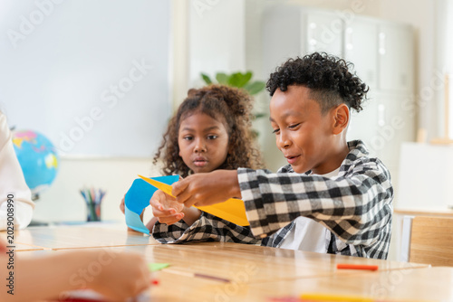 Diverse students making paper planes in a classroom, Happy children enjoying creative paper craft activity at school, Students learning and playing with colored paper in classroom