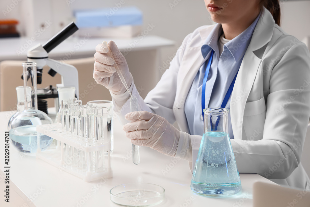 Fototapeta premium Female scientist dropping water sample into test tube at table in laboratory, closeup