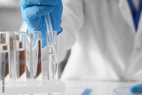 Female scientist dropping water sample into test tube at table in laboratory,...