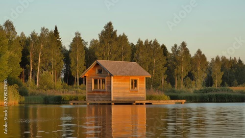 A small wooden cabin floating on a calm lake at sunset. Seamless looping 4k video background
