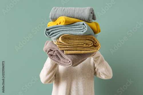 Obraz na plátně Young woman with stack of different blankets on turquoise background, closeup