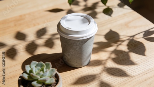 Minimalist paper coffee cup mockup on wooden table with elegant leaf shadows and succulent plant