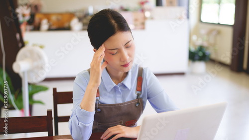 Asian women small business owner working cafe using laptop computer checking order manage restaurant shop entrepreneur touching head feeling tired stress work