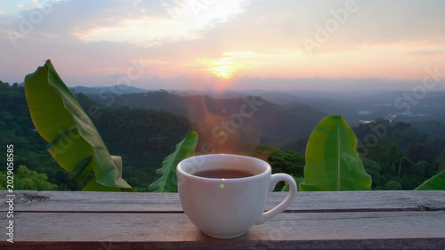 Hot cup of coffee on a wooden table overlooking tropical mountains at sunrise. Seamless looping 4k video background