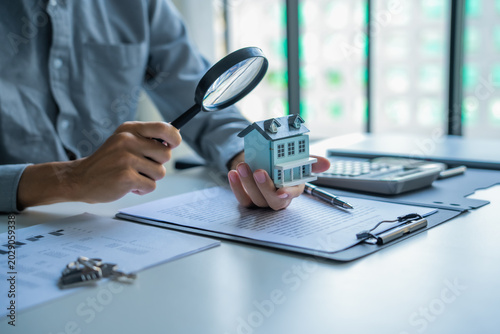 Asian businessman holding magnifying glass examine house model real estate invesment concept