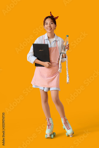 Young Asian smiling waitress on roller skates with menu and bottle of water o...