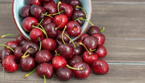 Ripe red cherries glistening with water spills from a blue ceramic bowl onto a dark wooden table, rustic summer freshness
