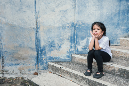 Принти на полотні Portrait of a sad Asian little girl sulking and sitting on steps against a grunge blue wall backdrop, showcasing childhood emotions, lonely feelings, and psychological expression concepts