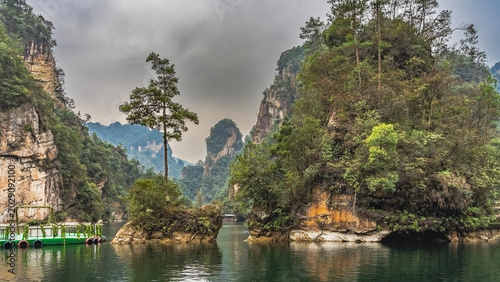 A calm and beautiful lake. Picturesque cliffs with green vegetation rise above the water. A floating recreation platform. Clouds in the sky. China.  Baofeng Lake. Wulingyuan
