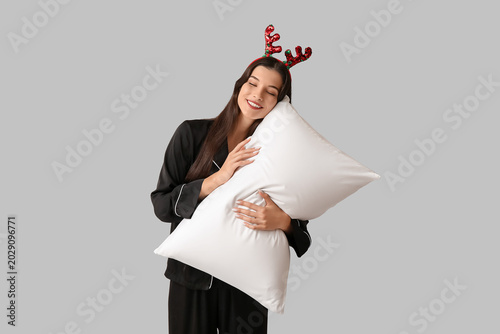Beautiful young woman in black pajamas and reindeer horns with soft pillow on...