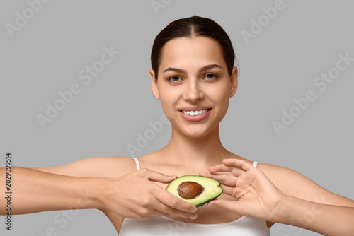 Pretty young woman with fresh avocado on grey background
