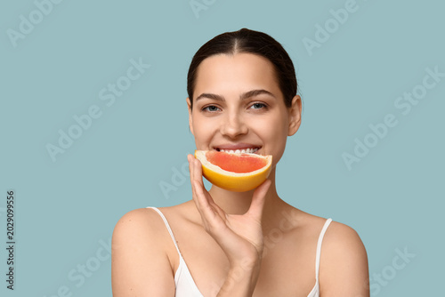 Pretty young woman with fresh grapefruit on blue background