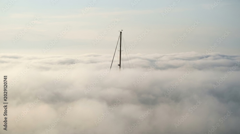 Fototapeta premium Towering Structure Piercing Through a Sea of Thick, White Clouds.