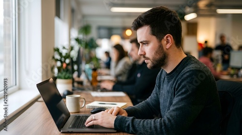 Focused professional man working on laptop in modern office environment near window.
