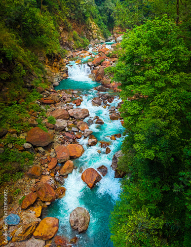 Vibrant turquoise water of Rimbi River flowing over orange boulders in West Sikkim,
India