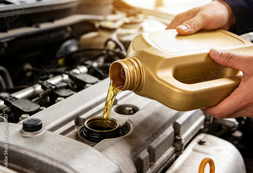 A close-up shot of a person's hands pouring fresh golden engine oil from a bottle into a car engine, highlighting routine vehicle maintenance.