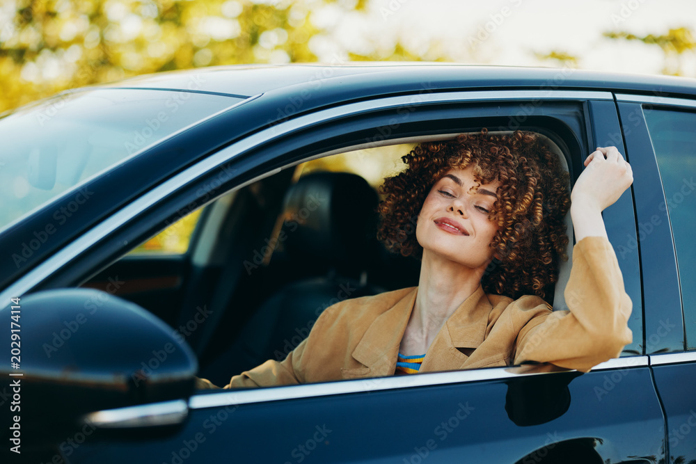 Fototapeta premium A cheerful woman drives a car with a relaxed smile, natural light in the cabin, and a retro film vibe. Concept for lifestyle joy and travel in a candid automotive moment.