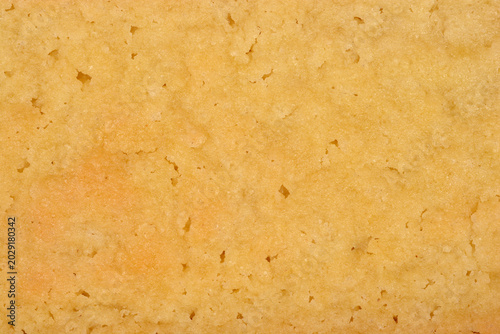 Macro background of a golden baked shortbread biscuit surface showing a crumbly porous texture made from butter flour and sugar.